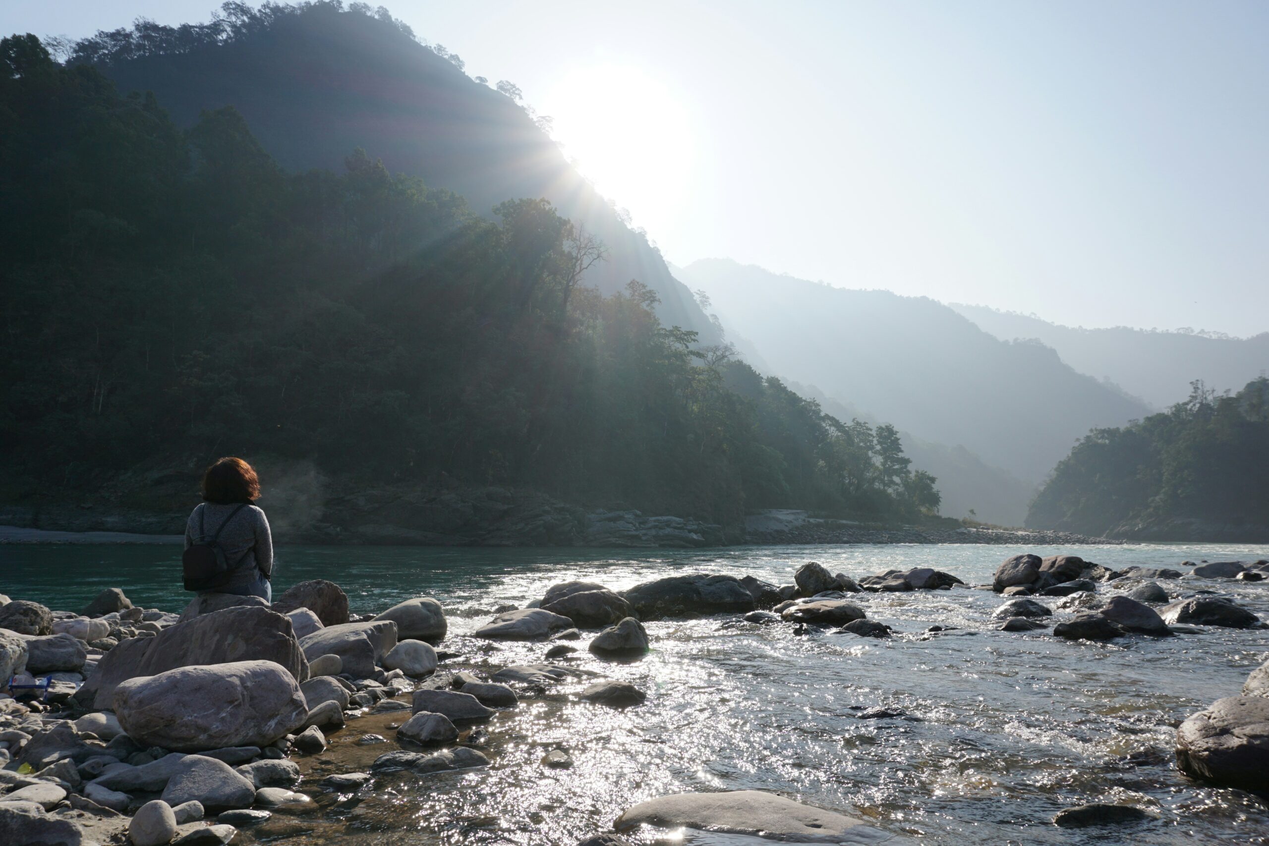 a person sitting on a rock near a river