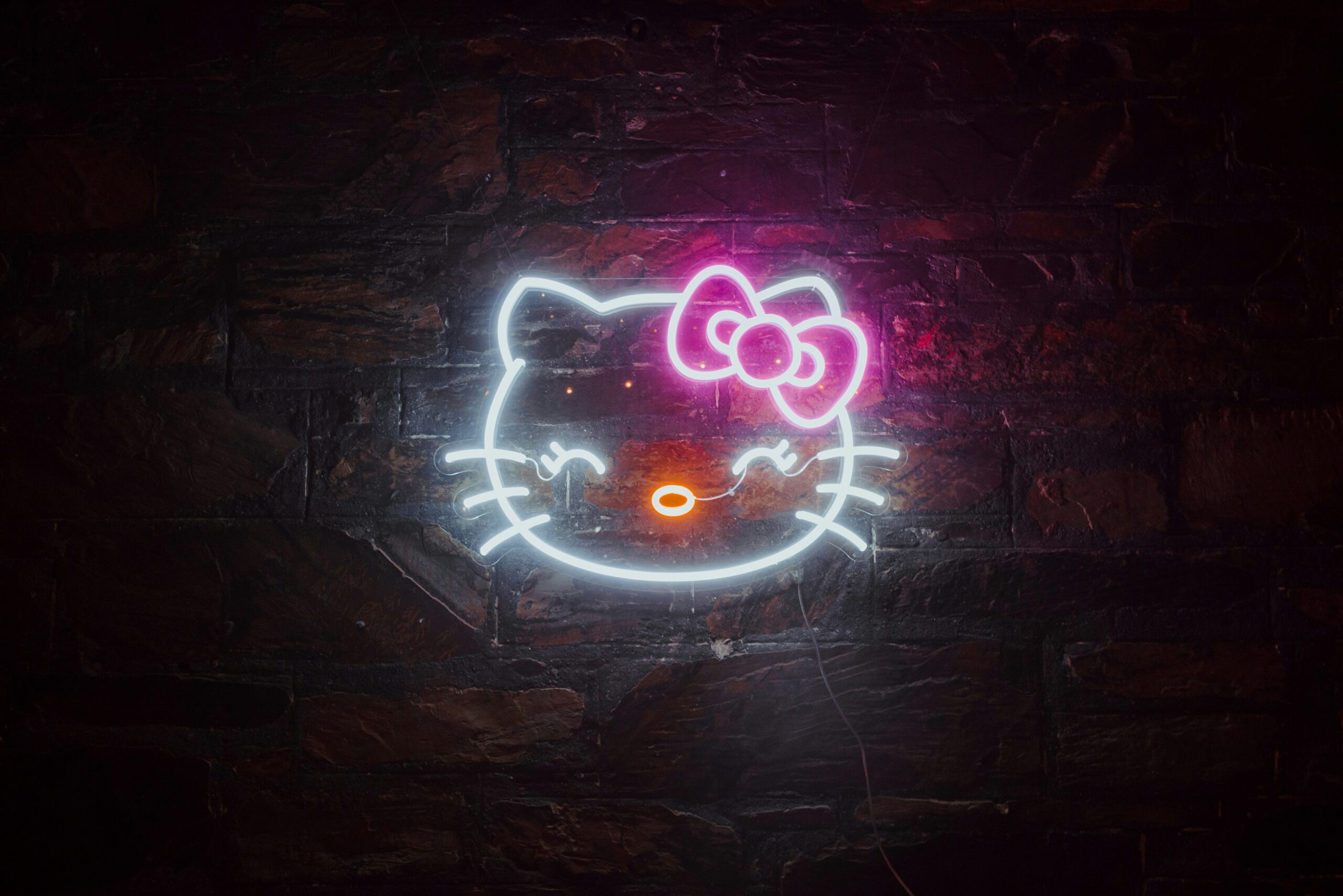 a neon hello kitty sign on a brick wall