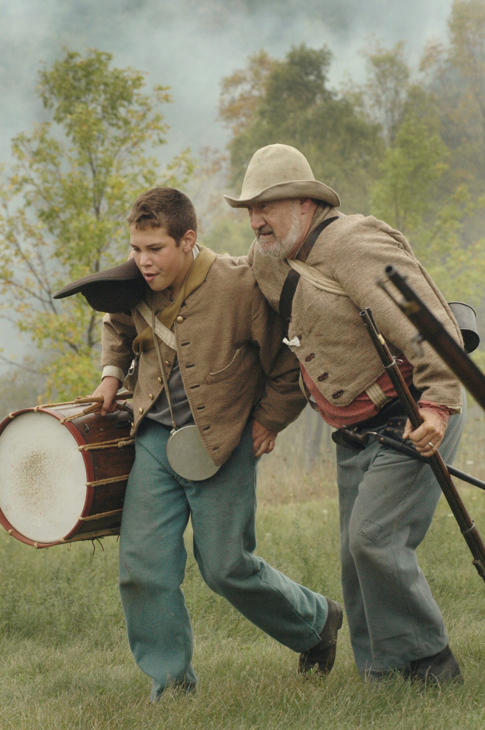 two men walking holding percussion instrument and rifle