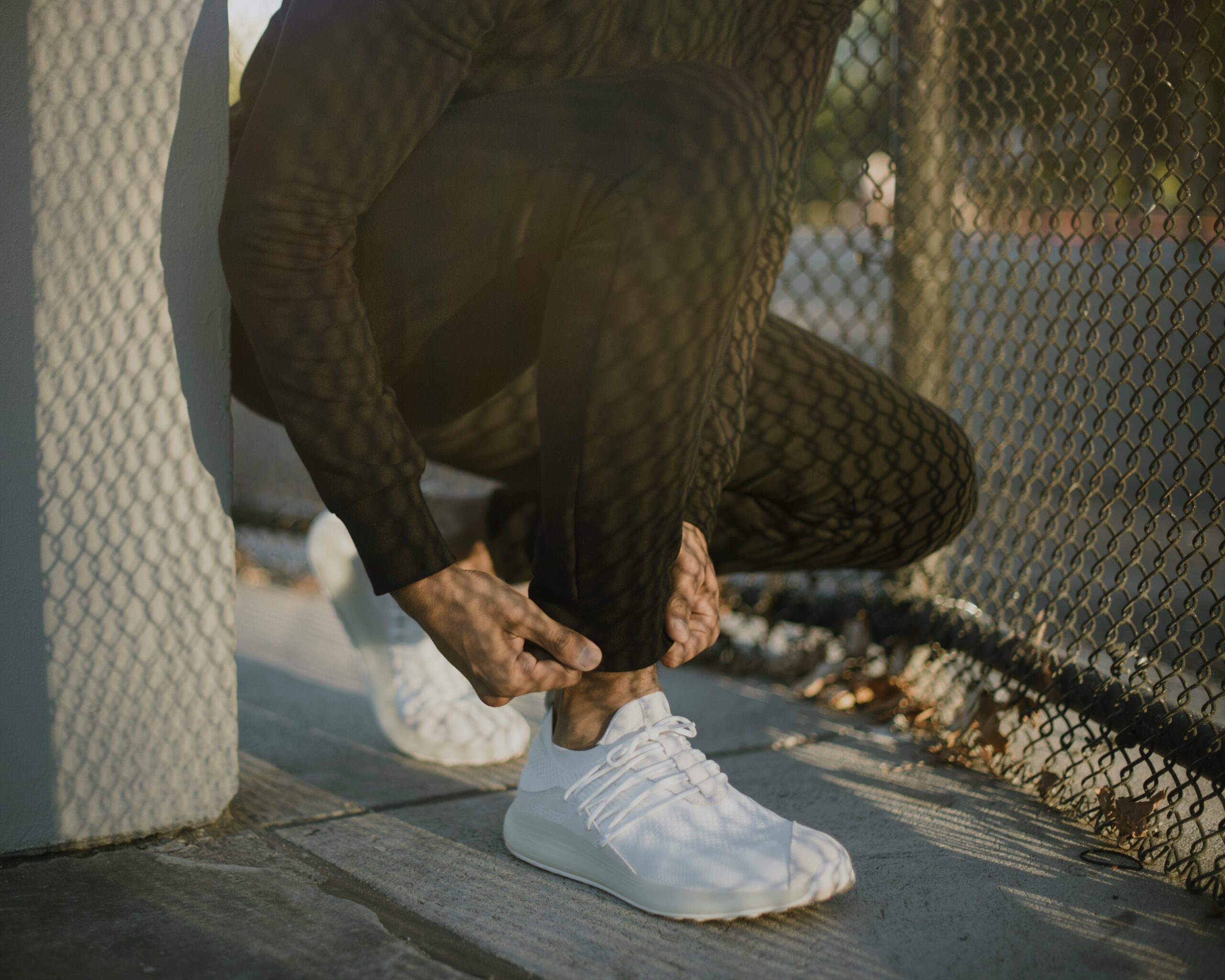 a man tying his white tennis shoes on the sidewalk