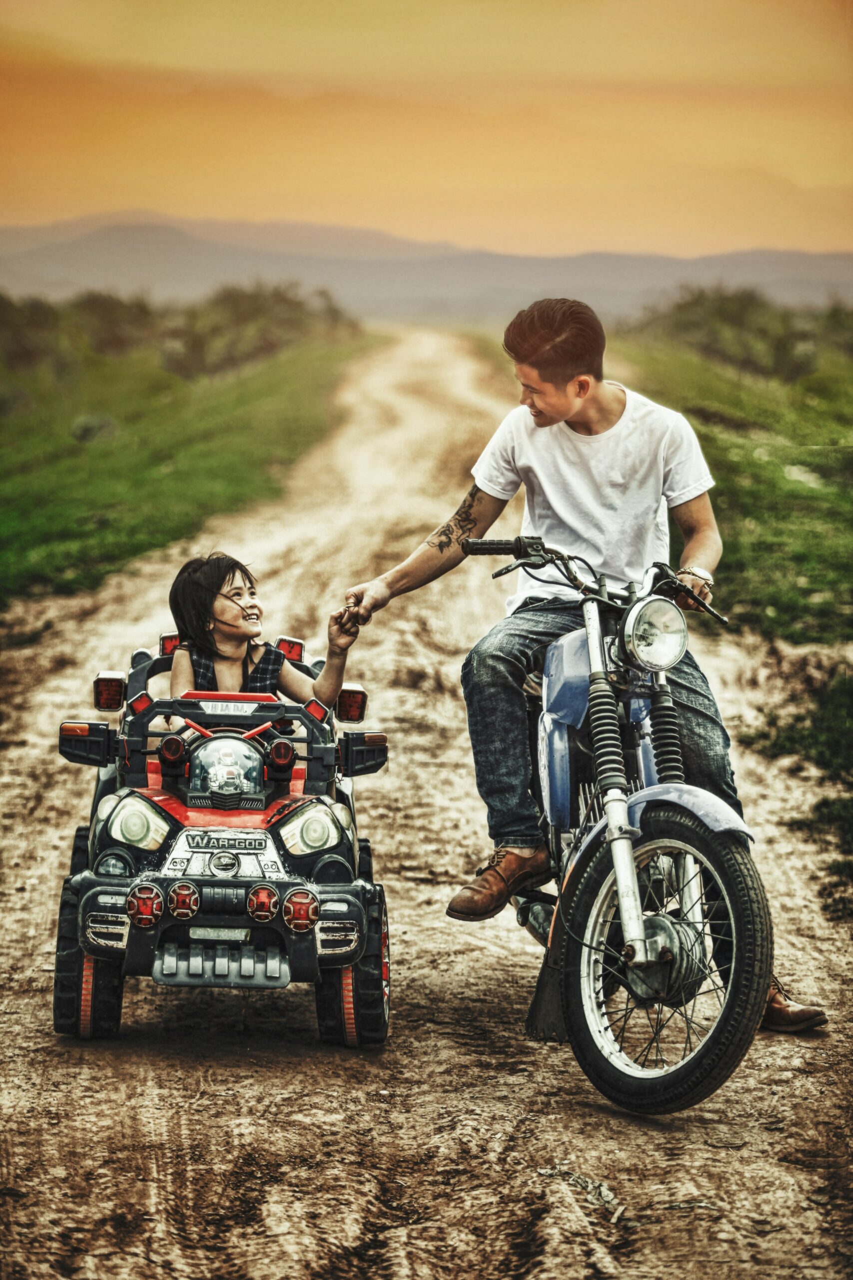 man riding motorcycle and toddler on a toy car in a road during daytime